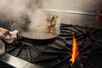 Cropped hand tossing vegetables in cooking pan over stove in kitchen at home