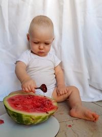 Little boy sitting on the floor and eating a red watermelon with a spoon, caucasian child