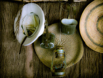 Old-fashioned lantern with hat and bottle hanging on thatched wall