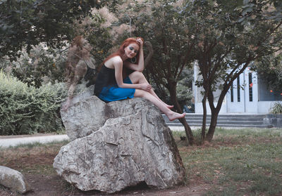 Woman sitting on rock against trees