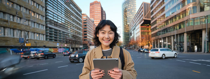 Portrait of young woman using mobile phone in city
