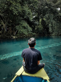 Rear view of man sitting on boat against lake