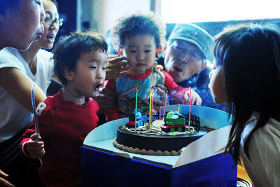 Boy blowing birthday candles with family at home