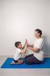 Grandmother and her grandson are sitting on a yoga mat in a white apartment at home