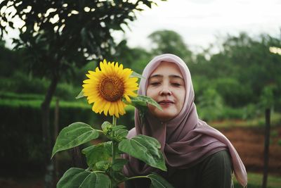 Portrait of smiling young woman with sunflower against plants