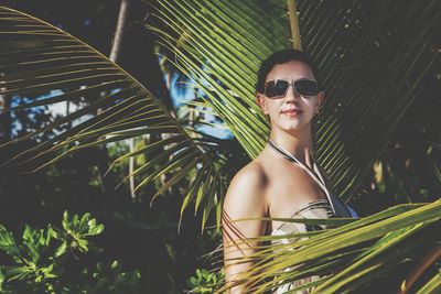 Woman in sunglasses standing by coconut palm tree