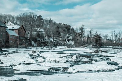 Frozen river by houses against sky