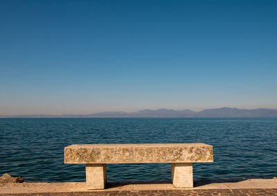 Scenic view of lake garda against clear blue sky with a stone bench