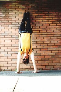 Rear view of woman on footpath against brick wall