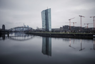 Bridge over river by buildings against sky