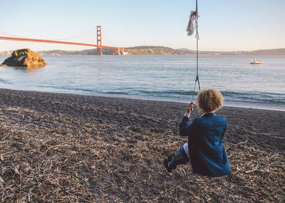 Rear view of woman sitting on swing with golden gate bridge in background