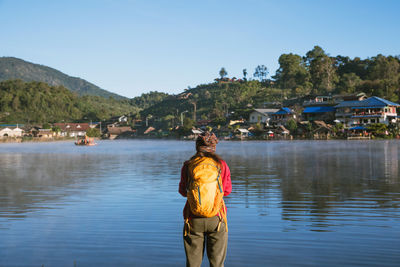 Rear view of man standing by river against sky