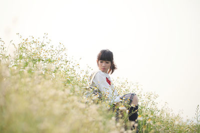 Woman looking away while sitting amidst plants on field