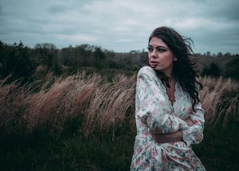 Portrait of beautiful woman standing on field against sky