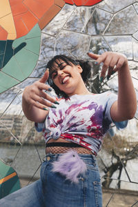 Low angle portrait of happy young woman gesturing while standing against mosaic wall