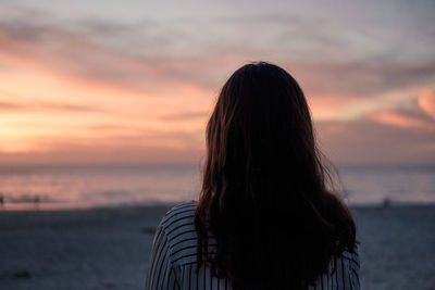 Rear view of woman against sea during sunset