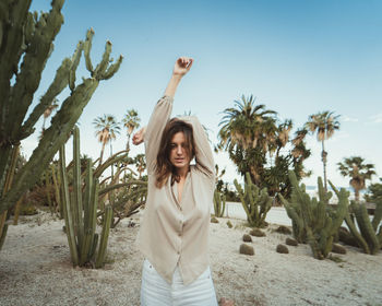 Tranquil female standing with raised arms in garden with various green cacti and looking at camera