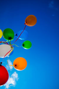 Low angle view of colorful balloons flying against blue sky