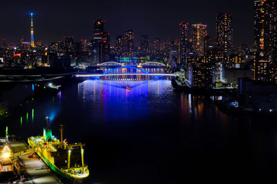 Illuminated city by river against sky at night