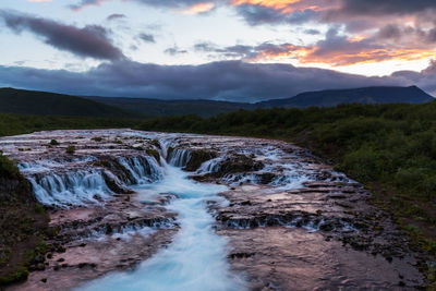 Scenic view of waterfall against sky during sunset