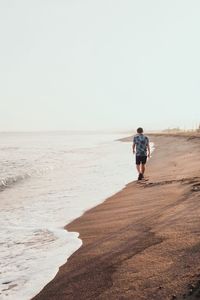 Rear view of man walking on beach against clear sky