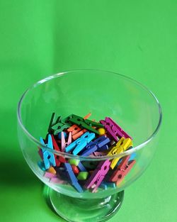 High angle view of multi colored clothespin in bowl against green background