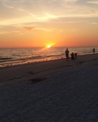 Silhouette people on beach against sky during sunset