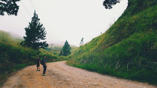 Men hiking on dirt road by green mountains against sky