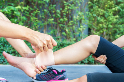 Cropped hands of person wrapping bandage on woman leg against plants