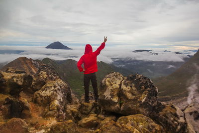 Man gesturing peace sign while standing on rock against sky