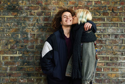 Woman kissing boyfriend while standing against brick wall