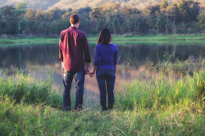 Rear view of women standing on grass by lake