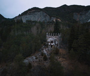 Scenic view of abandoned house by forest against sky