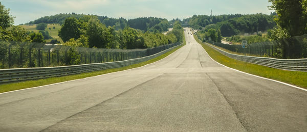 Empty road amidst trees against sky