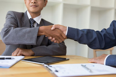 Midsection of businessmen shaking hands at desk in office