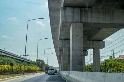 Road by bridge in city against sky