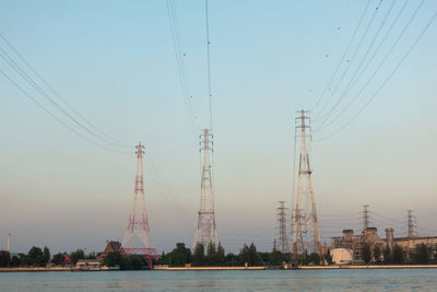 Cranes by electricity pylon against sky