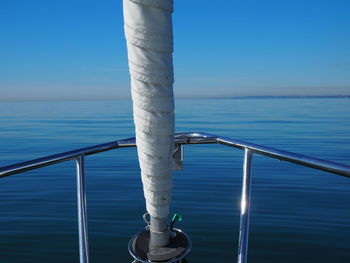 Railing by sea against blue sky and furled headsail