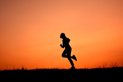 Silhouette of woman running on field at sunset