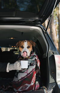 Cropped hand of woman holding coffee cup in front of car trunk