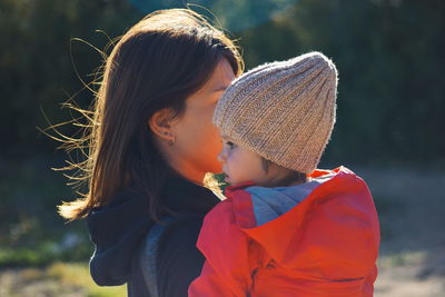 Side view of mother carrying daughter outdoors