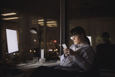 Businesswoman text messaging on smart phone sitting at work place