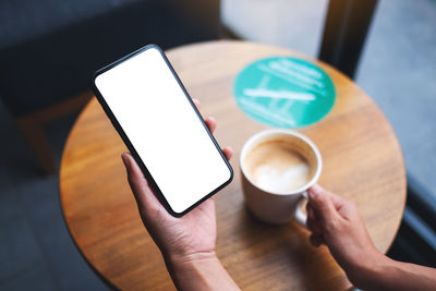 Mockup image of a woman holding mobile phone with blank white desktop screen while drinking coffee