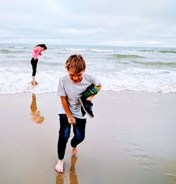 Siblings at beach against sky