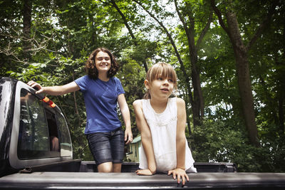 Sisters standing in pick-up truck against trees