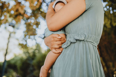 Midsection of woman holding hands while standing by tree