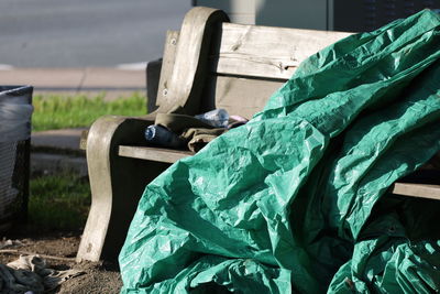 Close-up of green tarp on bench covered in trash