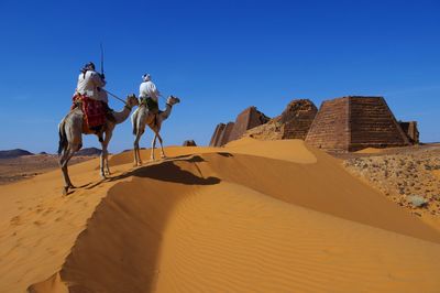 Rear view of woman walking on sand at desert against clear blue sky