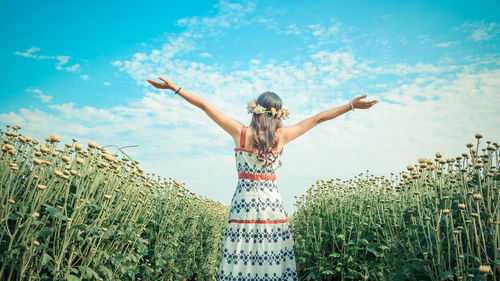 Woman with arms raised standing on field against sky