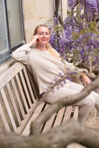 Beautiful middle-aged woman sits on a bench in the thickets of blooming wisteria